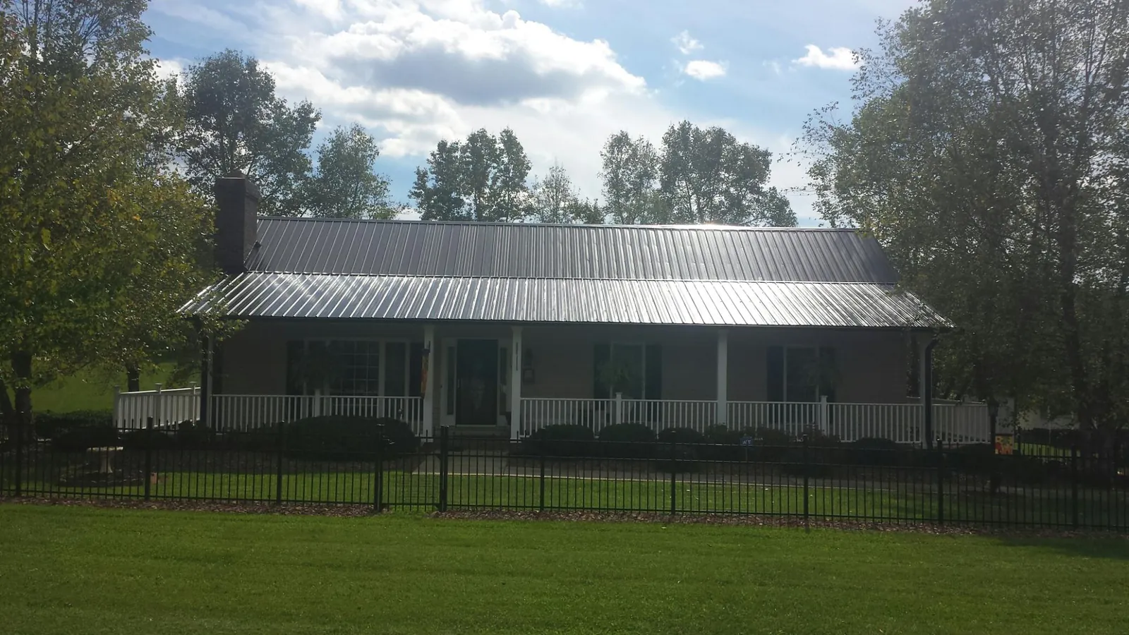 Gray metal roof on a brick ranch with a full width front porch — Gutter Guard Installation work by our crew in Oakfield