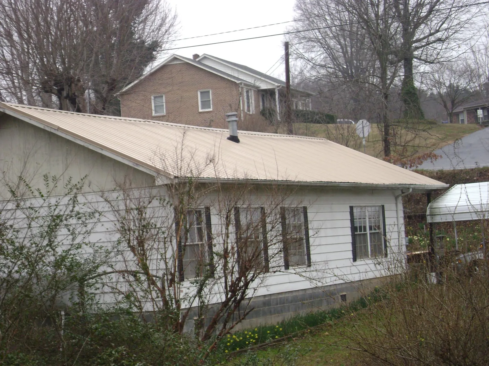 Tan metal roof on a white sided house set into a hillside — Commercial Roofing by Roofing Brothers in Oakfield